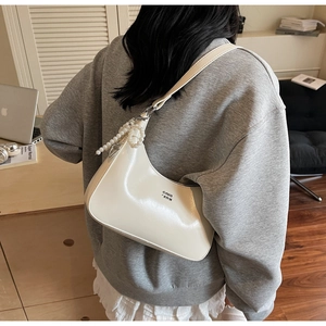 Detail of cream white patent leather hobo bag with pearl zipper charm and glossy finish