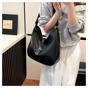 Detail of a large black tote bag featuring a decorative strap and metallic buckle on leather