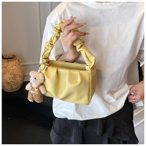 Close-up of yellow pleated cloud bag with a cute brown teddy bear charm accessory