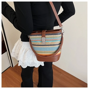 Detail of colorful rainbow woven straw bucket bag featuring brown leather trim and metal lock