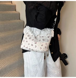 Detail of floral crossbody bag featuring red flowers and white lace trim on strap