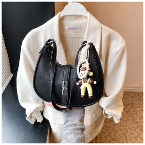 Close-up of black pebble leather half-moon bag with silver clasp and pearl doll charm