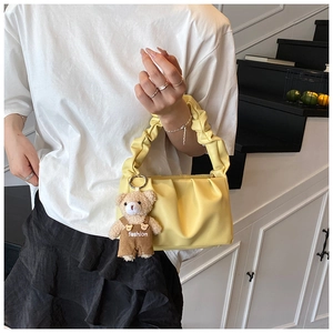 Detail of light yellow ruched shoulder bag with cute brown teddy bear charm accessory