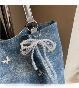 Detail of denim shoulder bag featuring silver butterfly accents and pearl lace bow charm