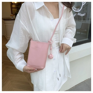 Detail of pink lychee leather phone bag with woven ball charm on a crossbody strap