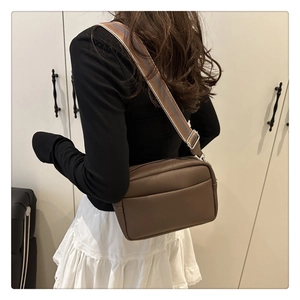 Detail of dark brown lychee leather crossbody bag with striped wide shoulder strap