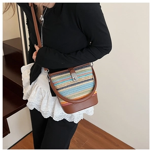 Close-up of rainbow straw woven bucket bag with brown leather strap and metal twist lock