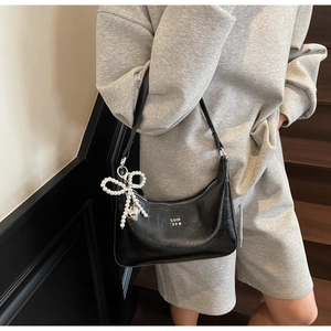 Detail of black patent leather bag with silver logo and pearl bow charm accessory