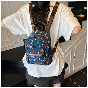 Detail of a denim mini backpack with colorful star patterns and brown leather trims