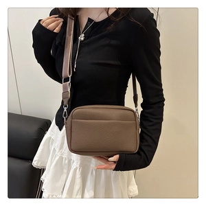 Brown lychee pattern crossbody bag with a wide striped fabric strap on a model