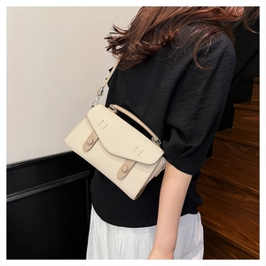 Beige textured square crossbody bag worn by a model in a modern indoor setting