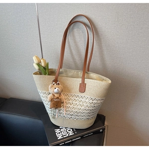 Detail of woven straw tote bag featuring leather straps and a brown plush bear charm
