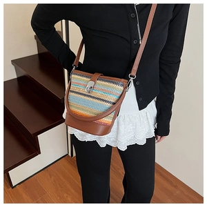 Close-up of rainbow straw bucket bag with brown leather trim and metal clasp on shoulder