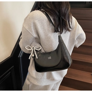 Detail of black faux leather dumpling bag with white pearl bow charm and shoulder strap