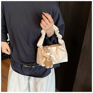 Detail of a creamy pleated shoulder bag featuring a cute teddy bear fashion charm