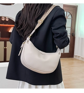 Detail of beige lychee grain leather crescent bag with adjustable wide woven shoulder strap