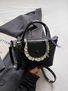 Chic black pleated mini bucket bag with lace trim and ribbon bow on a gray blazer background