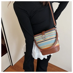 Side view of rainbow woven bucket bag with brown leather trim on female model