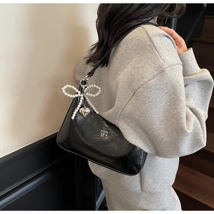 Detail of black glossy shoulder bag with pearl bow charm and silver heart pendant