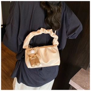 Chic cream pleated shoulder bag with a cute bear pendant worn by a model in a minimalist room