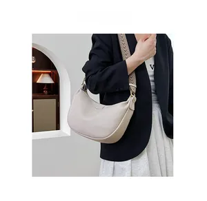 Detail of ivory dumpling bag featuring a wide woven strap and litchi grain leather
