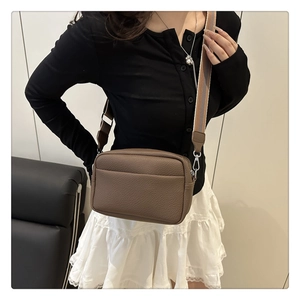 Close-up of brown litchi pattern PU leather crossbody bag with striped wide strap
