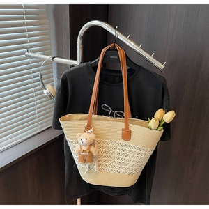 Detail of woven straw tote bag with brown leather straps and teddy bear pendant