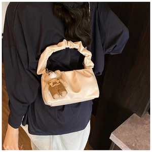 Detail view of cream pleated shoulder bag with cute teddy bear charm on model