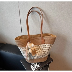 Detail of woven straw tote bag with brown leather straps and cute teddy bear charm accessory