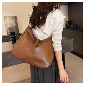 Detailed view of brown leather tote bag with decorative buckle on model in a modern room