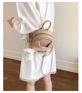 Mini beige cartoon cat backpack with plush charm worn on back in home setting