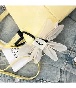 Detail of white flower fabric charm with FUOR label on a yellow leather bucket bag