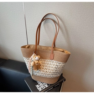 Detail of woven straw tote bag featuring contrast stitching and a cute bear charm