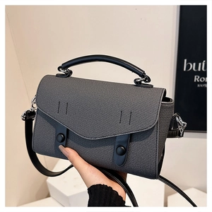 Close-up of gray textured crossbody bag with black leather handles and shoulder strap