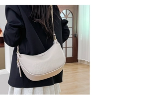 Detail of beige crescent bag with lychee texture and woven shoulder strap on model