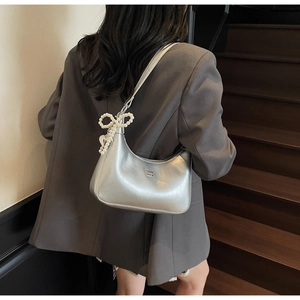Silver dumpling bag with pearl bow accessory shown on model in grey suit at stairs