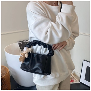 Detail of black pleated shoulder bag with bear charm and soft leather-like texture