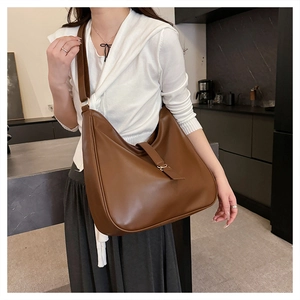 Brown leather large capacity hobo bag worn as a shoulder bag by a model in a modern room