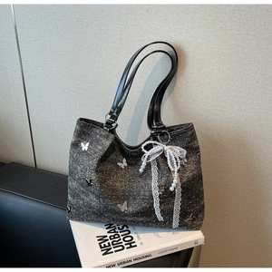 Detail of dark grey textured tote bag with silver butterfly charms and pearl bow