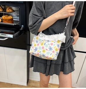 Detailed view of floral crossbody bag with white lace trim worn by model in a kitchen