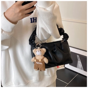 Detail of black pleated underarm bag with a brown plush bear charm and soft PU leather
