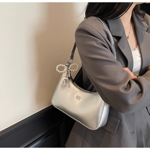 Detail of silver matte shoulder bag with pearl bow pendant and heart charm on a model