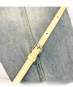 Detail of adjustable denim bag strap with yellow leather and silver metal buckle