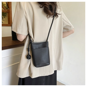 Close-up of black lychee grain leather crossbody phone bag with woven ball charm