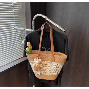 Detail of woven straw tote bag with brown leather straps and a small bear plush pendant