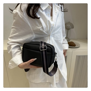 Detail of black lychee grain PU leather crossbody bag with striped wide shoulder strap