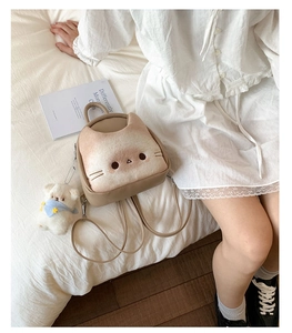 Close-up of a cute cat-shaped crossbody bag with a plush bear charm on white bedding