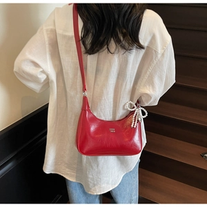 Detail of bright red glossy shoulder bag featuring pearl bow charm and COIH '2DN logo