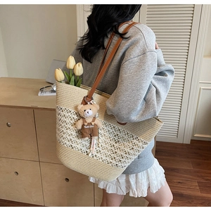 Close-up of beige straw tote bag with brown leather handles and teddy bear charm