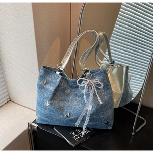 Detail view of blue denim tote bag with silver chain, butterfly motifs and lace bow
